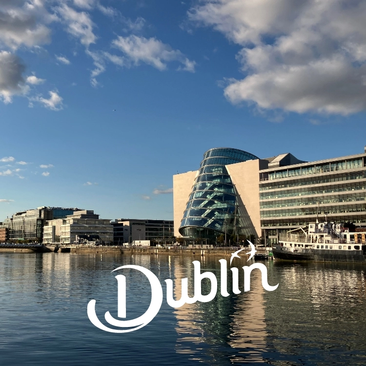 Modern glass building by the water in Dublin, under a blue sky with scattered clouds. The word “Dublin” in stylized white text is overlaid on the image.
