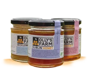 Three jars of Olly’s Farm honey are displayed, each labeled differently: Wicklow Honey, Dublin Honey, and Heather Honey. The jars have black lids and are arranged on a yellow circular mat.